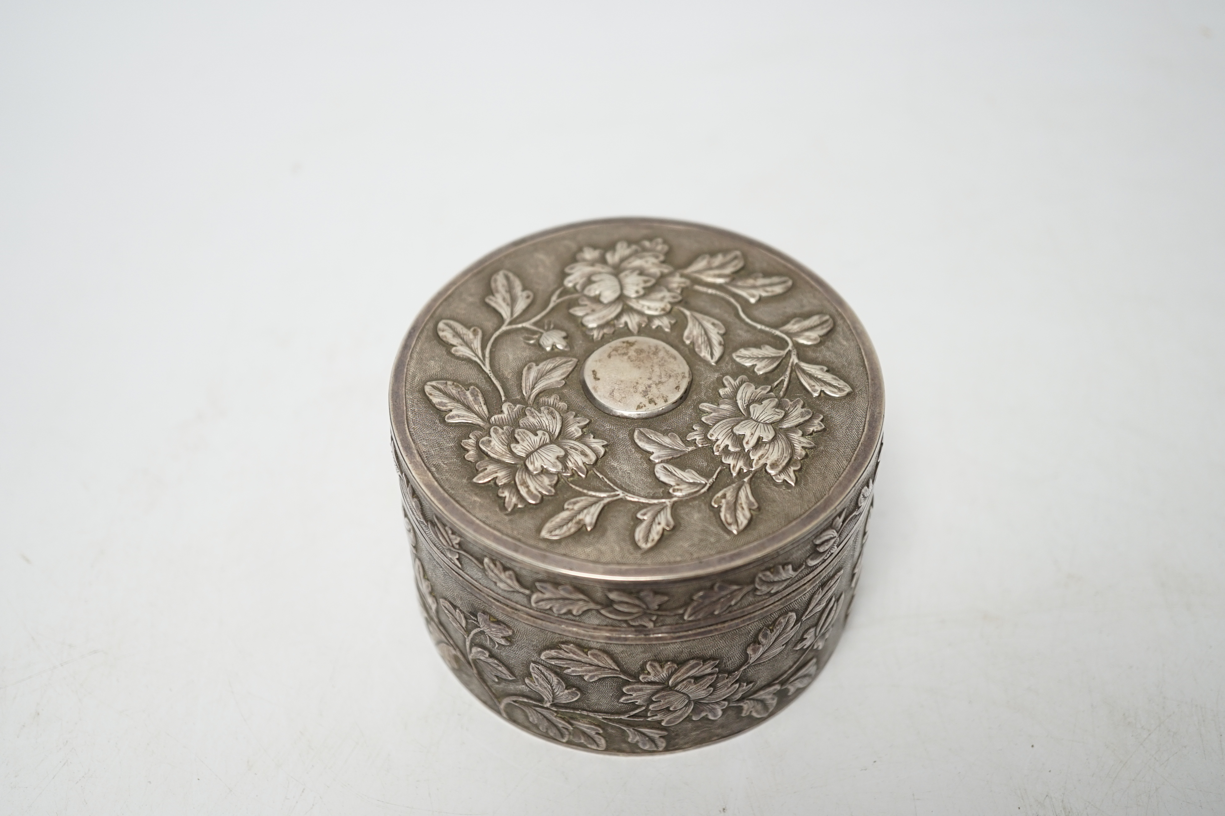 An early 20th century Chinese white metal circular box and cover, maker's mark MK, with foliate decoration and engraved inscription, diameter 82mm, 128 grams.